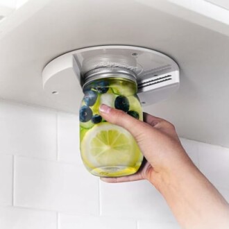 Hand using under-cabinet jar opener with a jar of lemon and blueberry drink.